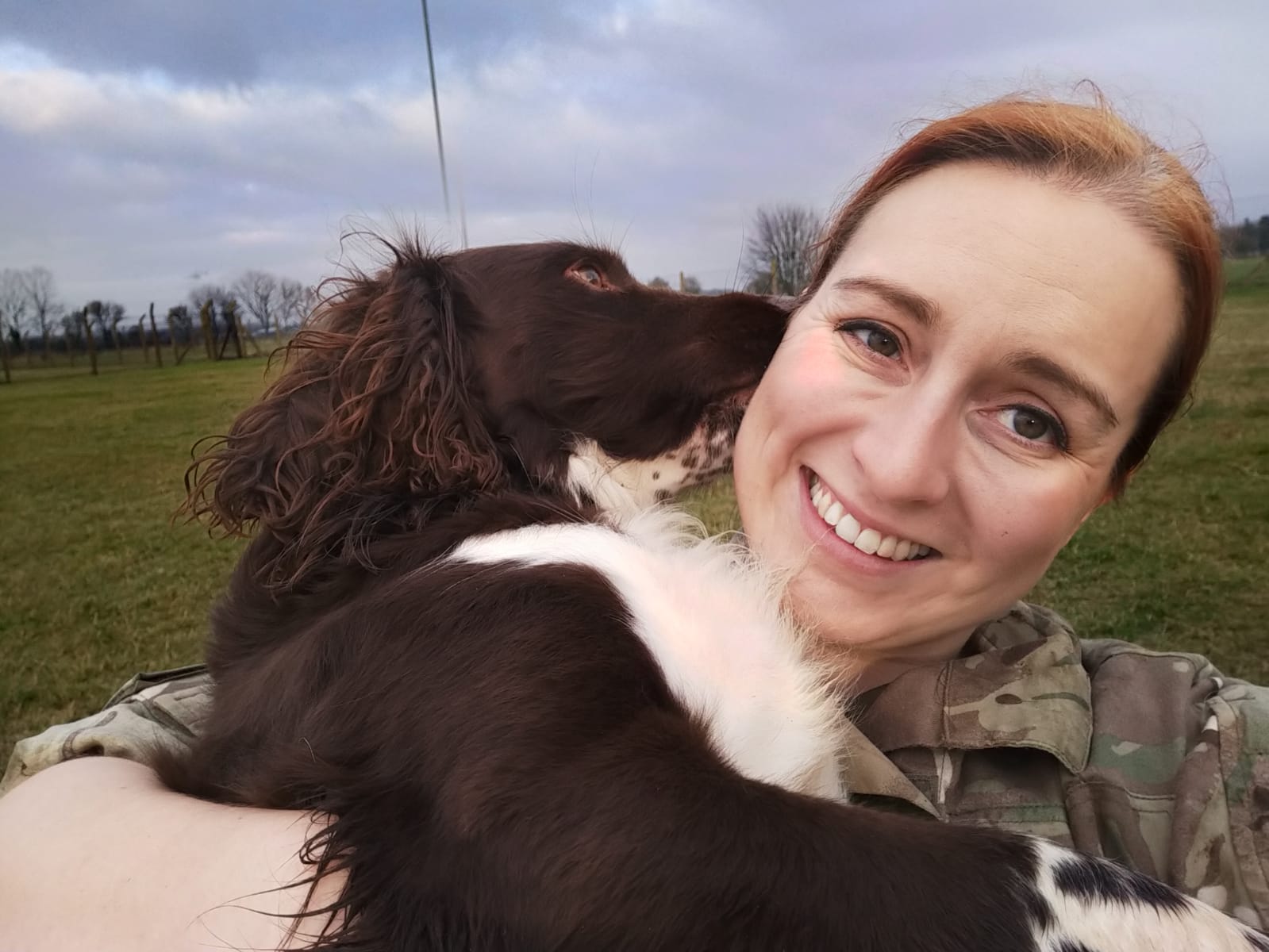 RAF Dog Handler cuddles dog, who licks her ear.